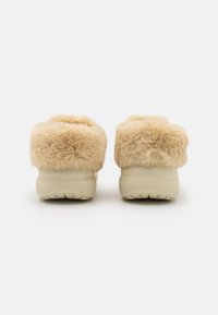 Chaussons beige duveteux avec une texture douce semblable à de la fourrure, dotés d'une semelle en caoutchouc léger et robuste et d'un design épuré.