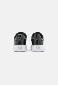 Sneakers in pelle verniciata nera con suole bianche. Caratterizzati dal logo "GUESS" in rilievo sul tallone e da un accento metallico circolare sul lato.