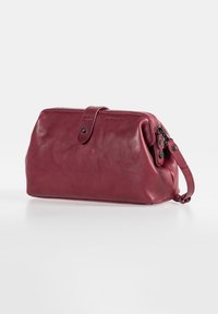 Burgundy leather bag with a rounded shape, top clasp closure, and a detachable wrist strap. Smooth texture and subtle hardware accents.