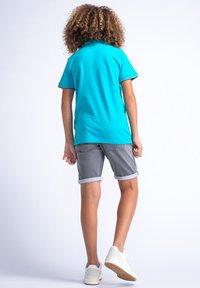 Tyrkysové polo tričko s krátkými rukávy, šedé vykroucené šortky a bílé tenisky. Hladká tkanina a klasický střih s kontrastními detaily.