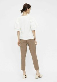 Haut blanc à manches courtes avec des manches bouffantes superposées, associé à un pantalon beige fuselé et des mules à talons beiges. Texture de tissu lisse.