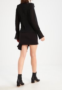 Top nero a maniche lunghe con pizzo alle estremità, abbinato a una mini gonna nera con orlo arricciato e stivaletti neri con tacco spesso.