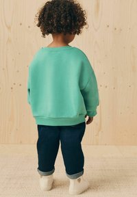 Felpa over size turchese con polsini a coste abbinata a jeans di denim scuri arrotolati all'orlo e sneakers bianche con dettagli a forma di cuore.