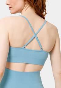 Svetle modrá sportovní podprsenka s žebrovaným vzorem a křížovými ramínky na zadní straně, širokým pasem a otevřenou částí dole pro lepší ventilaci.