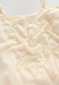 Perlenbloemen camisole in lichtbeige, met delicate borduursels en kleine pailletten, en verstelbare spaghettibandjes. Zachte, gladde textuur.