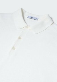 Valkoinen polo paita, joka on valmistettu teksturoidusta kankaasta. Paidassa on klassinen kaulus, kolme nappia ja etiketti näkyvissä kauluksessa.