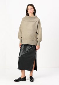 Pull beige oversize avec un col côtelé, associé à une jupe midi en cuir noir avec une fente sur le côté, et des mocassins noirs.