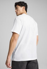 Camiseta de algodón blanca con mangas cortas, cuello redondo y un corte holgado, combinada con jeans oscuros grises. Diseño minimalista, sin logotipos visibles.