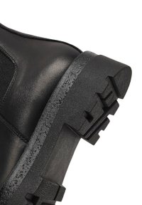 Stivale alla caviglia in pelle nera con finitura opaca, dotato di una suola in gomma spessa e di un motivo a trama testurizzata sul fondo per garantire aderenza.