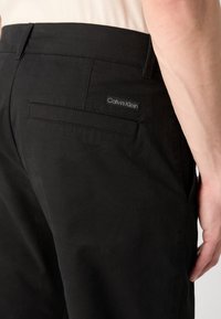 Pantaloni in cotone neri con tasca posteriore e etichetta con logo Calvin Klein, vestibilità tailored e texture liscia.