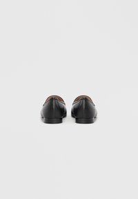 Scarpe nere in pelle con texture liscia, punta arrotondata, tacco basso e design minimalista. Vista posteriore che evidenzia cuciture sottili.