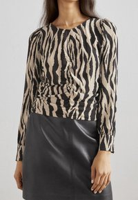 T-shirt à manches longues en imprimé zèbre beige et noir avec détail froncé sur le côté. Présente un col rond et un tissu extensible et lisse.