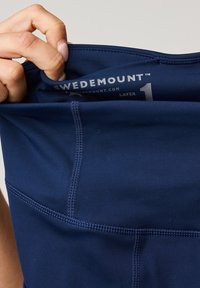 Granatowa sportowa bluzka z gładkiego materiału, płaskimi szwami oraz metką z napisem "SWEDEMOUNT" i "LAYER 1" wewnątrz dekoltu.