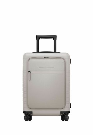 Light gray hard-shell suitcase with front zip pocket, four black spinner wheels, and black telescoping handle extended.