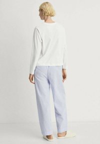 White long-sleeve top paired with light blue and white striped pajama pants. The outfit has a relaxed fit, with soft texture throughout.