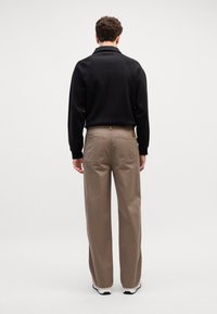 Mustard pullover ribiga tekstuuriga, koos khaki pükstega, millel on kaks tagataskut. Riietust täiendab valge soolaga tossud.