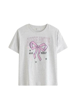 Teenagepige med langt blondt hår iført en grå T-shirt med et pink sløjfe-design, sort nederdel, hvide sokker og sølvfarvede sneakers.