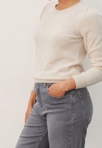 Jasnobeżowy, miękki sweter z bufkami na ramionach, zestawiony z szarymi dżinsami z klasycznymi kieszeniami. Sweter ma ściągacze na mankietach i na dole.