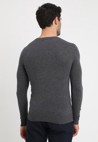 Pull gris charbon en tissu tricoté doux. Il présente un col rond et un ourlet côtelé, avec des manches longues et une silhouette ajustée.