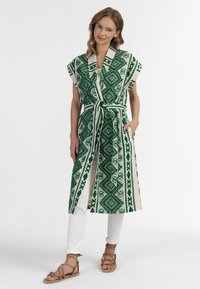 Zaļš un balts rakstots garais veste ar īsām piedurkn�ēm, jostu vidukļa līmenī un kabatām, apvienots ar baltām biksēm un brūnām siksniņu sandalēm.