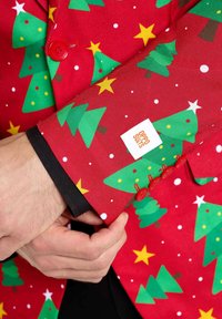 Rode blazer met een patroon van groene kerstbomen, gele sterren en witte stippen. Inclusief rode knopen en een wit label met "OPPO SUITS."