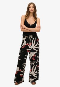 Pantalones de pierna ancha negros con un patrón de hojas tropicales en blanco y rojo, confeccionados en una tela ligera y con un corte holgado.