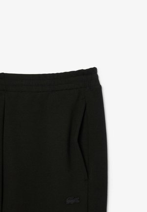 Black sweatpants featuring an elastic waistband, side pockets, and a small black logo on the left thigh. Smooth texture, casual design.