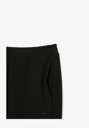 Schwarze Jogginghose mit elastischem Bund, Seitentaschen und kleinem schwarzem Logo am linken Oberschenkel. Glatte Textur, lässiges Design.