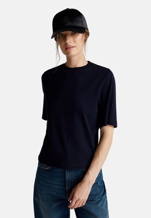 Camiseta de manga corta azul marino hecha de material suave, con cuello redondo y un ajuste relajado, combinada con una gorra de cuero negra.