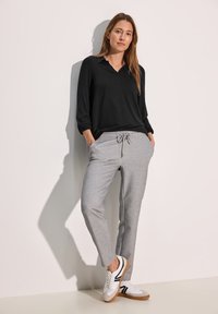 Schwarzes Langarmoberteil, graue Sweatpants mit Kordelzug und weiße Sneakers mit schwarzen Akzenten. Glattes Material und lockere Passform.