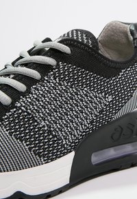 Černé a šedé pletené tenisky s vzorovaným síťovaným svrškem, šedými tkaničkami a černou podrážkou s viditelnou vzduchovou jednotkou.