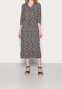 Zwarte bloemen midi-jurk met driekwart mouwen, v-hals en aansluitende taille, met roze en witte bloemenpatronen. Gecombineerd met zwarte sandalen.