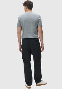 Zwarte cargobroek met zijzakken, gecombineerd met een grijs T-shirt met korte mouwen en witte sneakers, gezien van achter.