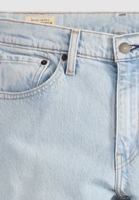 Svijetloplava traperice s dizajnom od pet džepova, bakrenim zakovicama i šivenim detaljima. Oznaka nosi natpis "Quality Clothing" na kvadratnoj naljepnici.
