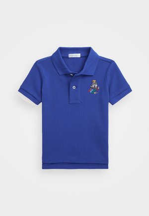 Polo azul de manga corta con cuello y dos botones, con un pequeño oso bordado que sostiene equipo deportivo en el pecho izquierdo.