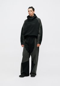 Conjunto deportivo negro y gris que incluye una sudadera con capucha de acabado texturizado y pantalones holgados con parches de contraste.