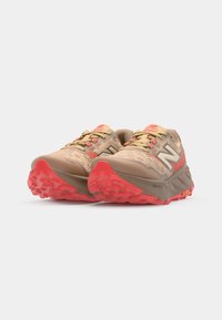 Lette beige trail running sko med mesh-overdel, røde accenter og tekstureret sål for godt greb. Indeholder en formet hæl og logo-detalje.