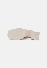 Heeled shoe with a white, textured sole; block heel and smooth upper. Sole features vertical lines for grip. Minimalistic design.