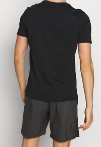Černé bavlněné tričko s krátkým rukávem, volný střih a kulatým výstřihem. Spárováno se šedými šortkami, viditelná textura a ležérní designové prvky.