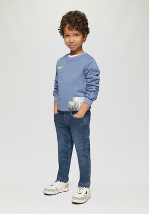 Lichtblauwe sweatshirt met de tekst "Moon in" gecombineerd met blauwe spijkerbroek. Witte sneakers met grijze accenten. Ontworpen voor casual wear.