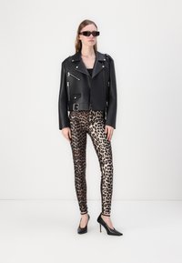 Crna kožna motorka jakna sa srebrnim patentnim zatvaračima, u kombinaciji s tajicama u leopard printu u smešnim i bež tonovima. Crne cipele s visokom petom, modernog dizajna.