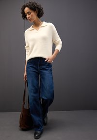 Maglione écru in maglia con scollo a V e maniche tre quarti; abbinato a jeans in denim a gamba larga blu e borsa a tracolla marrone.