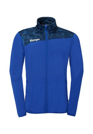 Blauwe sportjas met volledige ritssluiting en geometrisch donkerblauw patroon over de schouders, Kempa-logo op de linkerborst en een staande kraag.