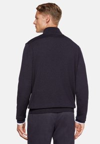 Navy knit jacket with a high collar, ribbed cuffs, and hem; features a textured pattern and a relaxed fit, designed for comfort.