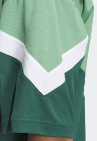 Lyhythihainen urheilupaita, jossa on teksturoitu pinta ja vihreät, valkoiset sekä tummanvihreät viuhkanmuotoiset väriosiot.