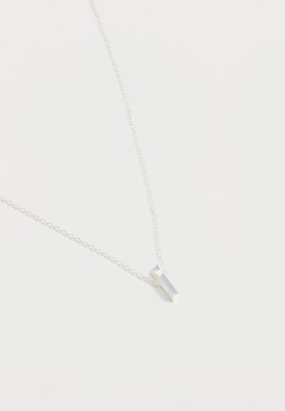 Collier fin en argent avec un petit pendentif barre verticale en argent sur un fond blanc uni.