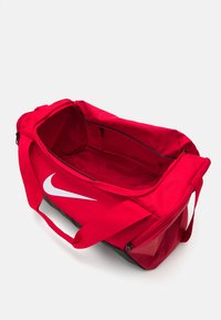 Rød duffelbag lavet af holdbart materiale med et stort, åbent indre. Har et fremtrædende hvidt Nike-logo og sorte lynlåsdetaljer.