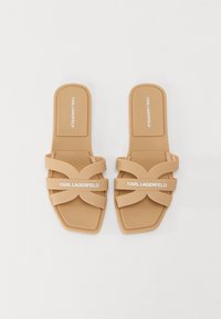 Tan rubber slide sandals with two crossed straps. Features "KARL LAGERFELD" logo in white on the strap. Square toe and flat sole design.
