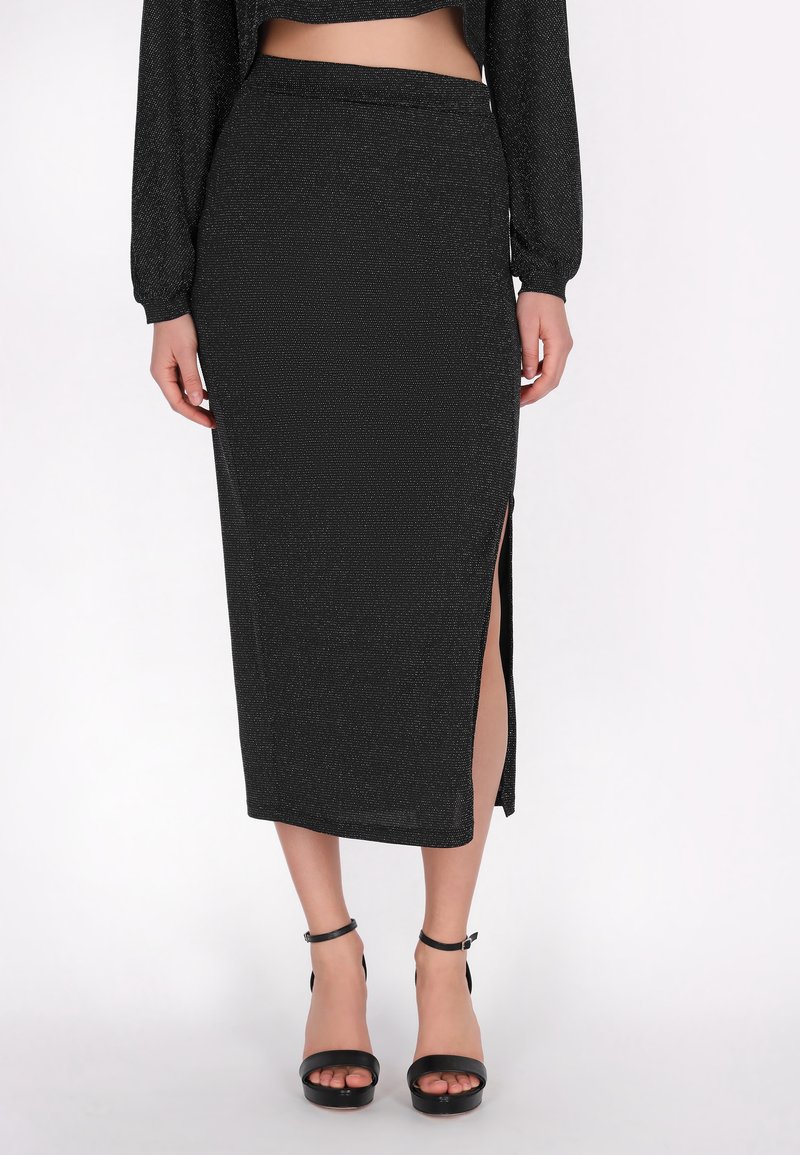 Czarna midi spódnica z bocznym rozcięciem, teksturowana tkanina z metalicznymi drobinkami i dopasowanym pasem w talii. W zestawie z czarnymi sandałami na obcasie.