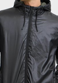 Schwarze, leichte Jacke mit glatter, glänzender Textur. Verfügt über einen durchgehenden Reißverschluss, eine verstellbare Kapuze mit Kordelzug und Nahtdetails.